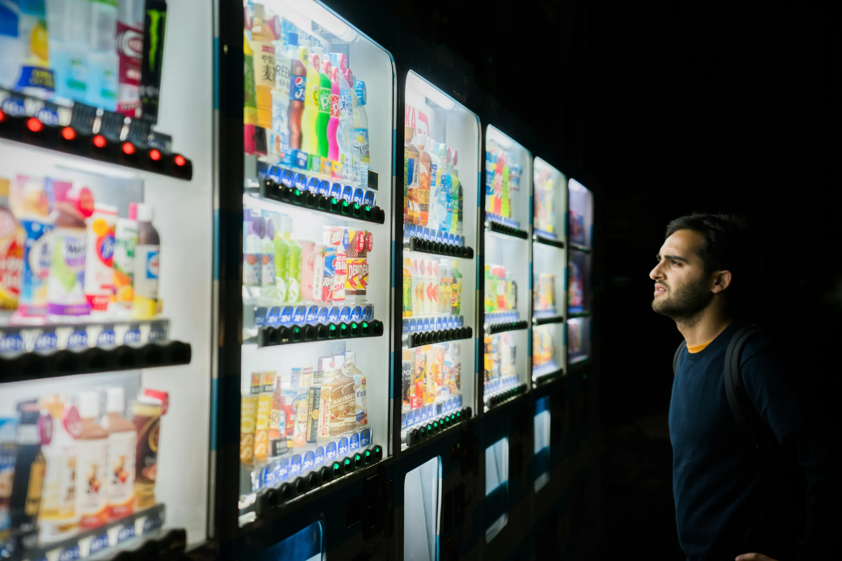 A person browsing a wall of illuminated smart vending machines at night